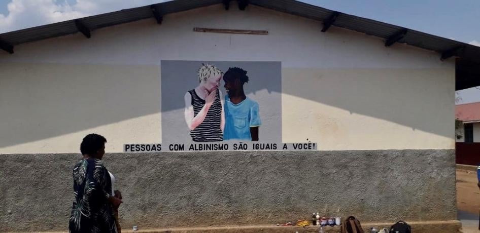Flavia Pinto, head of Azemap, a volunteer-run organization that supports people with albinism, stands before a mural painted at a school in Tete province. The mural reads: "People with albinism are the same as you!"