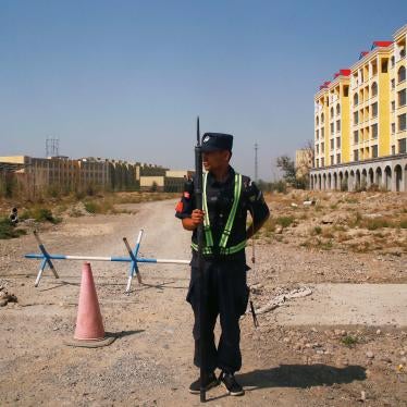 An armed police officer stands on a road leading towards a large yellow building