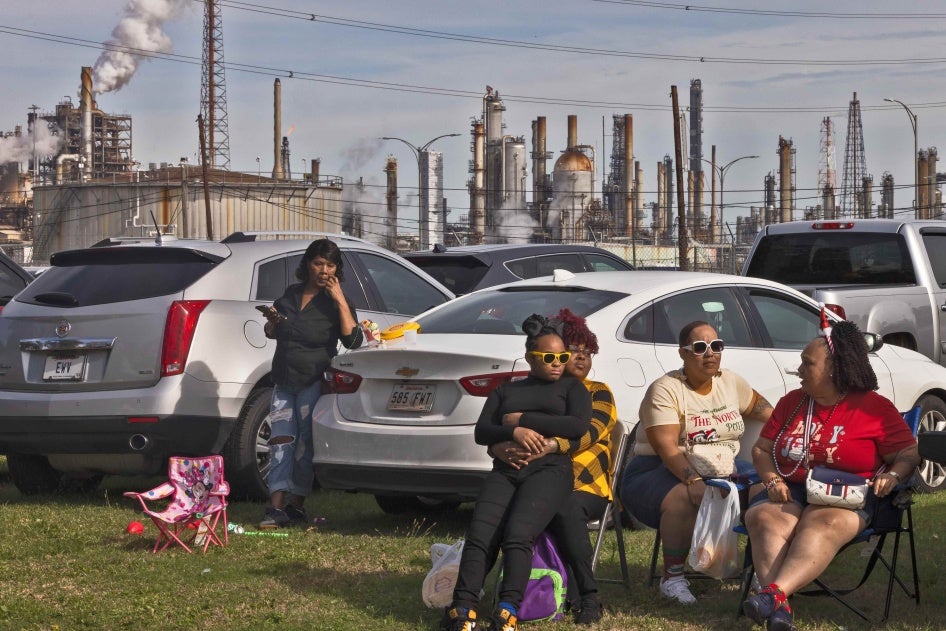 Residents of Louisiana’s Cancer Alley attend a Christmas Day parade while smoke and flares rise from fossil fuel and petrochemical plants behind them.
