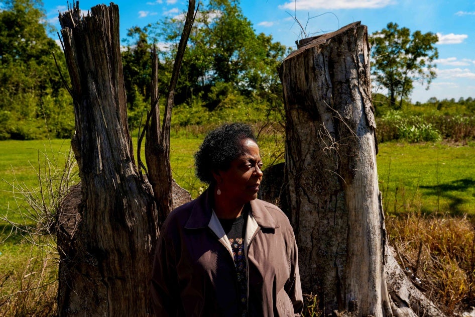 A woman stands in front of two dead trees