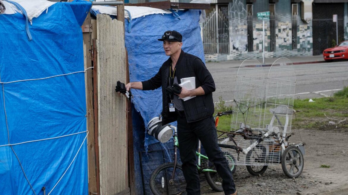 A man knocks on the door of a makeshift shelter covered in blue tarps.