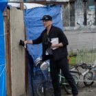 A man knocks on the door of a makeshift shelter covered in blue tarps.