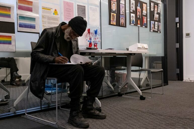 A man sits with a clipboard on his lap filling out forms.