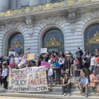 A rally at City Hall with a sign reading "Every Overdose Death Is a Policy Failure" #fundharmreduction