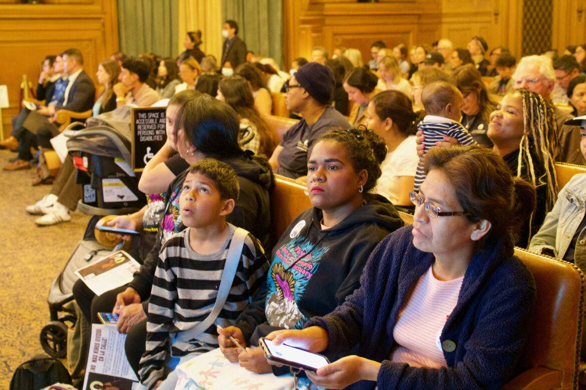 Homeless migrant families and others sit in City Hall Chambers during a meeting.