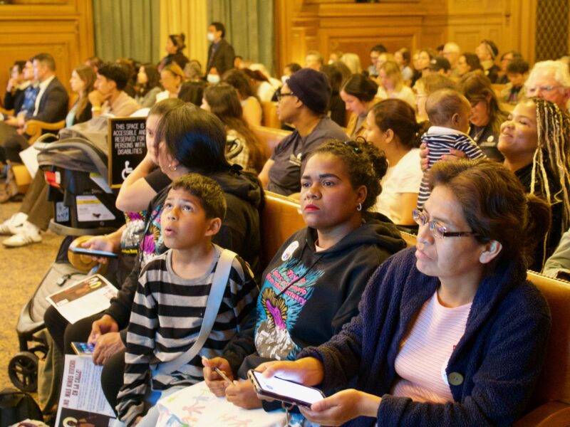 Homeless migrant families and others sit in City Hall Chambers during a meeting.