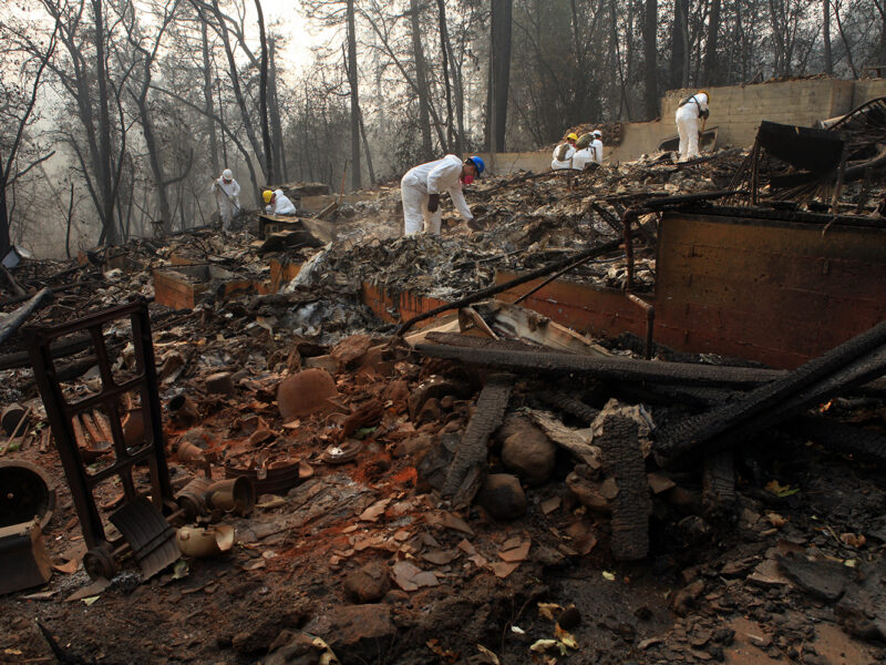 Workers in white suits sift through burned debris after the Camp Fire, the largest in California history.