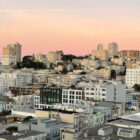 Dozens of buildings on Russian Hill are clustered together under a pink and orange sky.