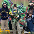 Three people stand and hold flowers and other harvest from Hummingbird Farm.