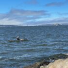 A kayaker paddles past Treasure Island as fog rolls in over the Presidio and Marin Headlands and across the Golden Gate Bridge into the San Francisco Bay.