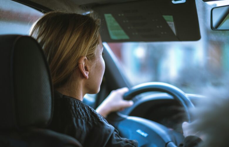 A woman sitting in a car, behind the steering wheel.