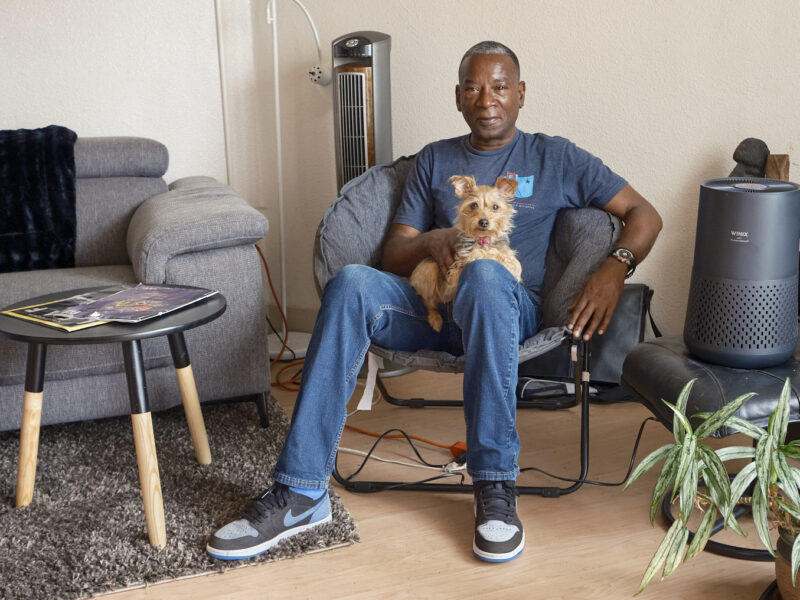 John Britt sits in his apartment with his dog on his lap, and his air purifier to his left.