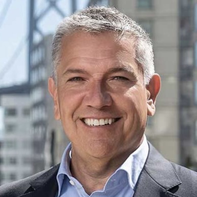 Closeup photo of Supervisor Matt Dorsey smiling at the camera. The background shows city buildings and part of the Bay Bridge.