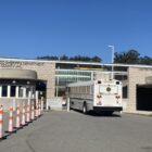 A San Francisco Sheriff's Department prisoner transport bus arrives at the San Francisco County Jail in San Bruno. The cream-colored bus is driving through the entrance, which is flanked by two brown brick walls. A series of tall, narrow traffic cones appear on the left side of the frame. District Attorney Brooke Jenkins criticizes the use of pretrial diversion programs offering defendants accused of selling drugs rehabilitation, counseling and training rather than jail sentences. Many such suspects are held at the San Francisco County Jail in San Bruno.