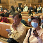 An interpreter speaks Cantonese into a device that transmits to listeners, with headsets, during a public meeting held in English.