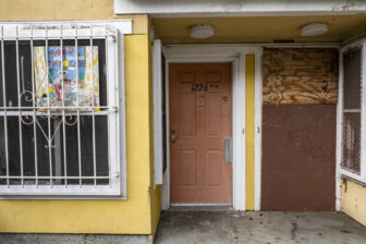 Two front doors to apartments at Plaza East, the one on the right boarded up.