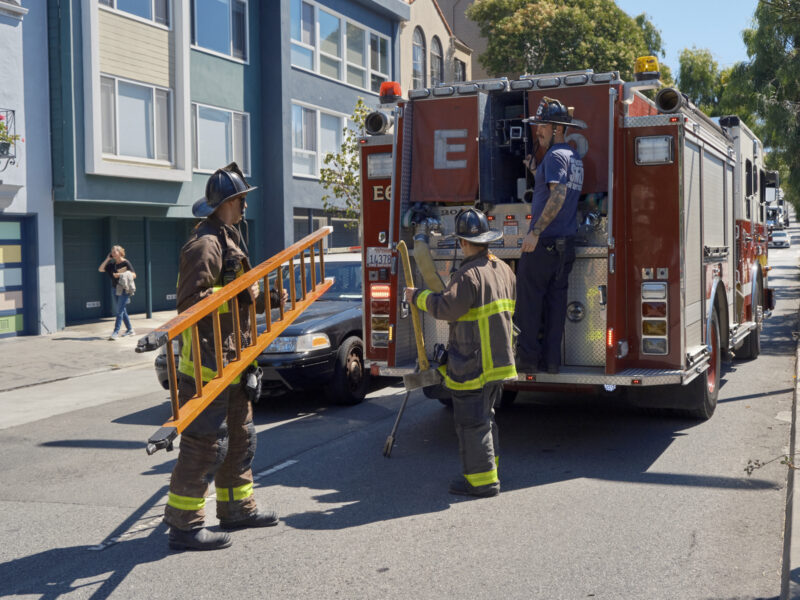 Firefighters handle a ladder and other gear in the field.