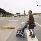 A woman crosses the street with a stroller and child at the intersection of Lincoln Way and the Great Highway.