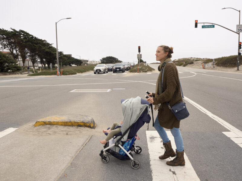 A woman crosses the street with a stroller and child at the intersection of Lincoln Way and the Great Highway.