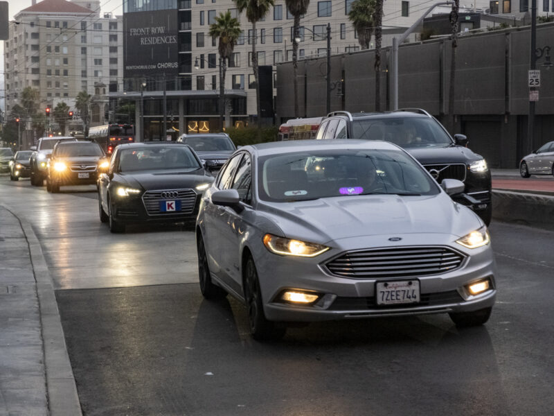 A car with a Lyft sign drives along a city street.