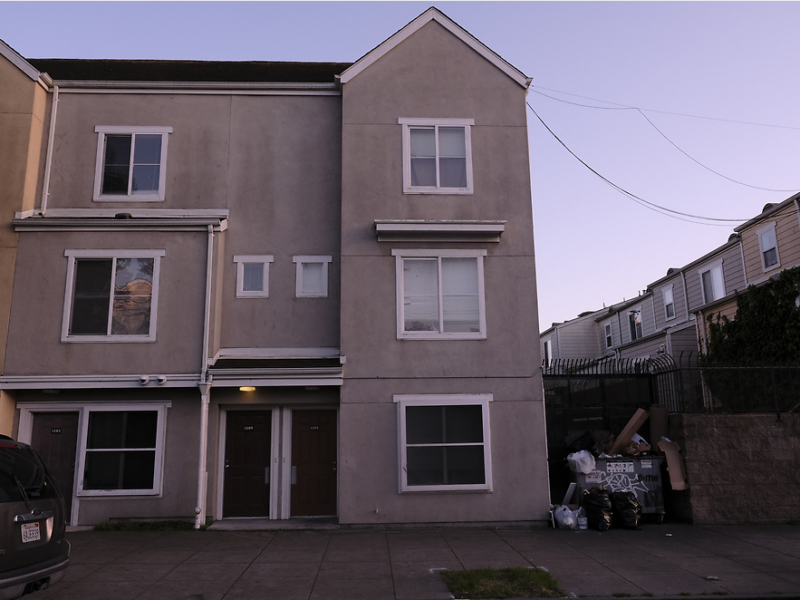 A street view of a complex of three-story apartment buildings.